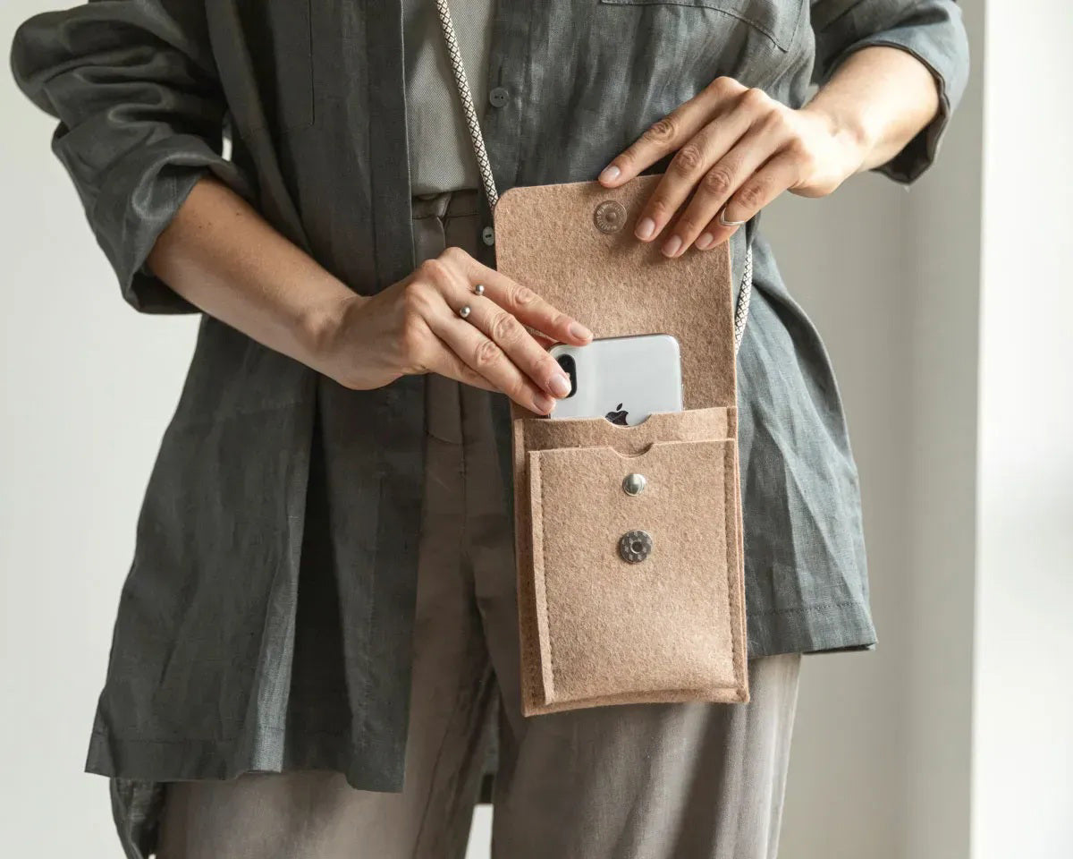 A person in a loose gray shirt and taupe pants carries the WOOLBERRY WOOL FELT PHONE BAG—a pink crossbody with a flap and silver chain—over their shoulder, showing only their torso and part of their arms.