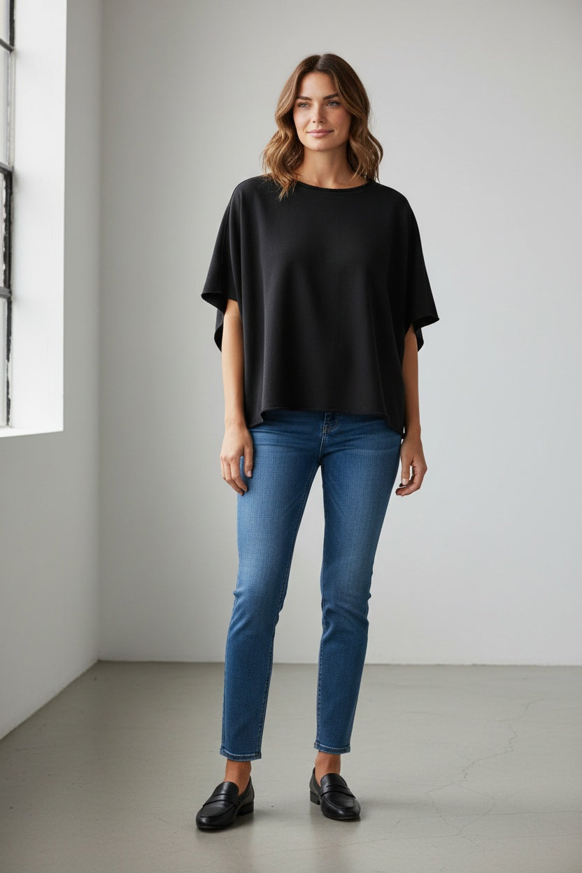 The FRANK & EILEEN OLIVE ORIGINAL CAPELET in black, by FRANK & EILEEN, is a black oversized T-shirt with a round neckline and short, wide sleeves. Made from 100% cotton, it features a loose fit and simple design reminiscent of a capelet against a light textured background.
