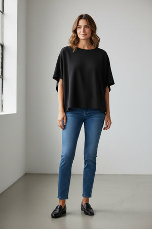 The FRANK & EILEEN OLIVE ORIGINAL CAPELET in black, by FRANK & EILEEN, is a black oversized T-shirt with a round neckline and short, wide sleeves. Made from 100% cotton, it features a loose fit and simple design reminiscent of a capelet against a light textured background.