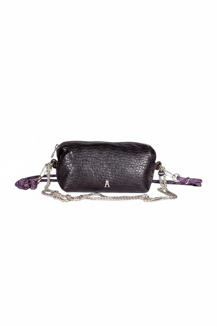 The CRAIE STUDIO - NUAGE BUBBLE POURPRE MINI BAG, a compact and textured black lambskin accessory featuring silver hardware and an eye-catching purple patterned strap, is showcased on a white pedestal against a plain background.
