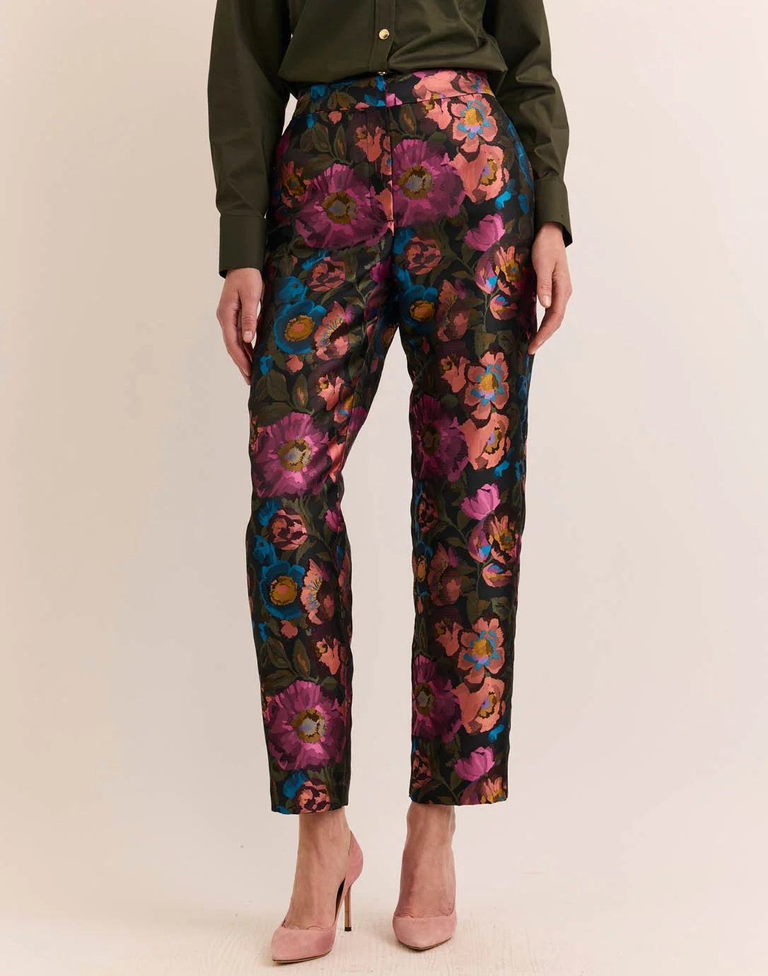 Dressed in the HINSON WU JOLENE JAQUARD PANT IN FLORAL BOUQUET, this person showcases high-waisted, straight-leg trousers with a bold pink, purple, blue, and orange floral print from HINSON WU, styled with an olive green top and light pink heels for a refined yet vibrant tailored ensemble.