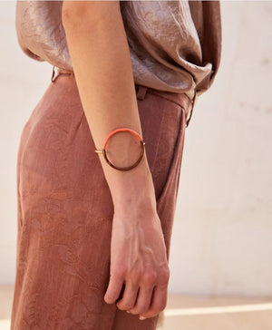The DIP DYE BRACELET by MOMONI is a uniquely designed artisanal piece, featuring an enamelled metallic golden band with a round, circular structure. The bracelet showcases an elegant combination of half brown and half light blue hues, boasting an irregular, organic shape and minimalist style, set against a plain white background.