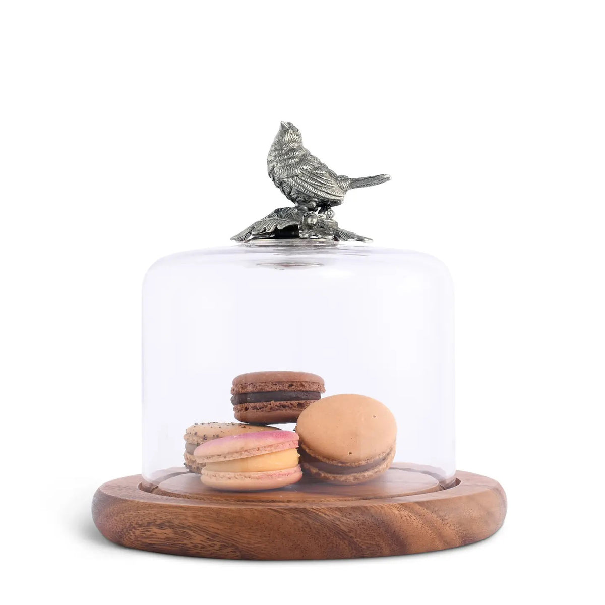 The VAGABOND HOUSE - SONG BIRD COVERED CHEESE BOARD elegantly displays four colorful macarons under a glass cloche topped with a bird figurine, all on a sophisticated wooden base.
