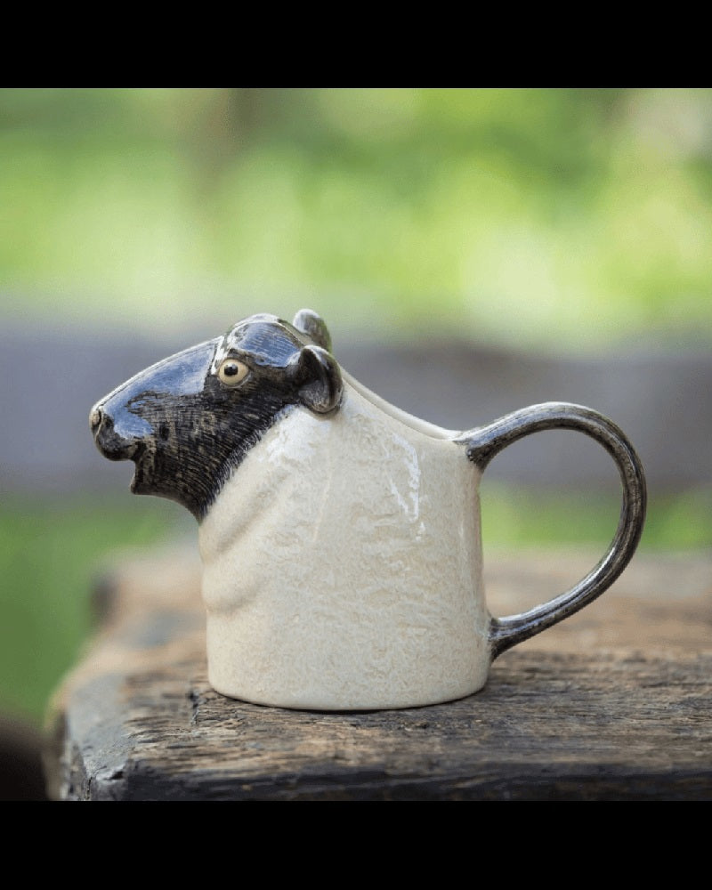 The QUAIL CERAMICS - BLACK SUFFOLK SHEEP JUG by QUAIL DESIGNS features realistic black ears, a black nose, and yellow eyes—perfect for adding farmhouse charm to your kitchen decor.