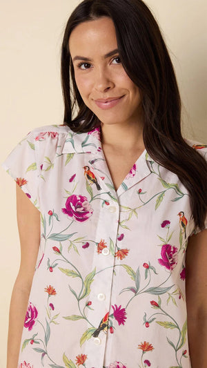 A person is wearing the CAT'S PAJAMAS ROSA AND BIRD LUXE PIMA COTTON PAJAMA SHORT SET, barefoot, standing against a plain background and looking to the side with a relaxed posture.