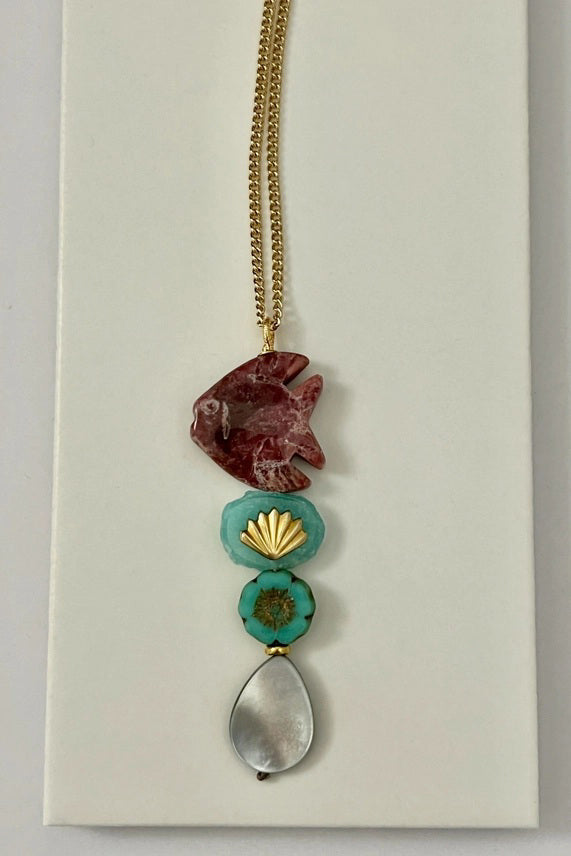 The SANDRINE FRANCE STUDIO - COMPANION LEO NECKLACE features a rhodonite fish pendant, two green Peruvian aventurine beads, and a teardrop-shaped gray stone on a gold chain—an elegant handmade piece from SANDRINE FRANCE STUDIO.