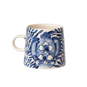 The CREATIVE COOP CREAM AND BLUE HAND-PAINTED STONEWARE MUG features a blue floral and leaf design on white, a handle, tapered shape, and glossy finish—bringing artisanal charm to your daily coffee.