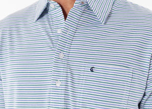 A person in sunglasses wears the CRIQUET Top-Shelf Players Shirt in Stewart Stripe White, standing by a countertop with a green can against blue-gray tiled walls.