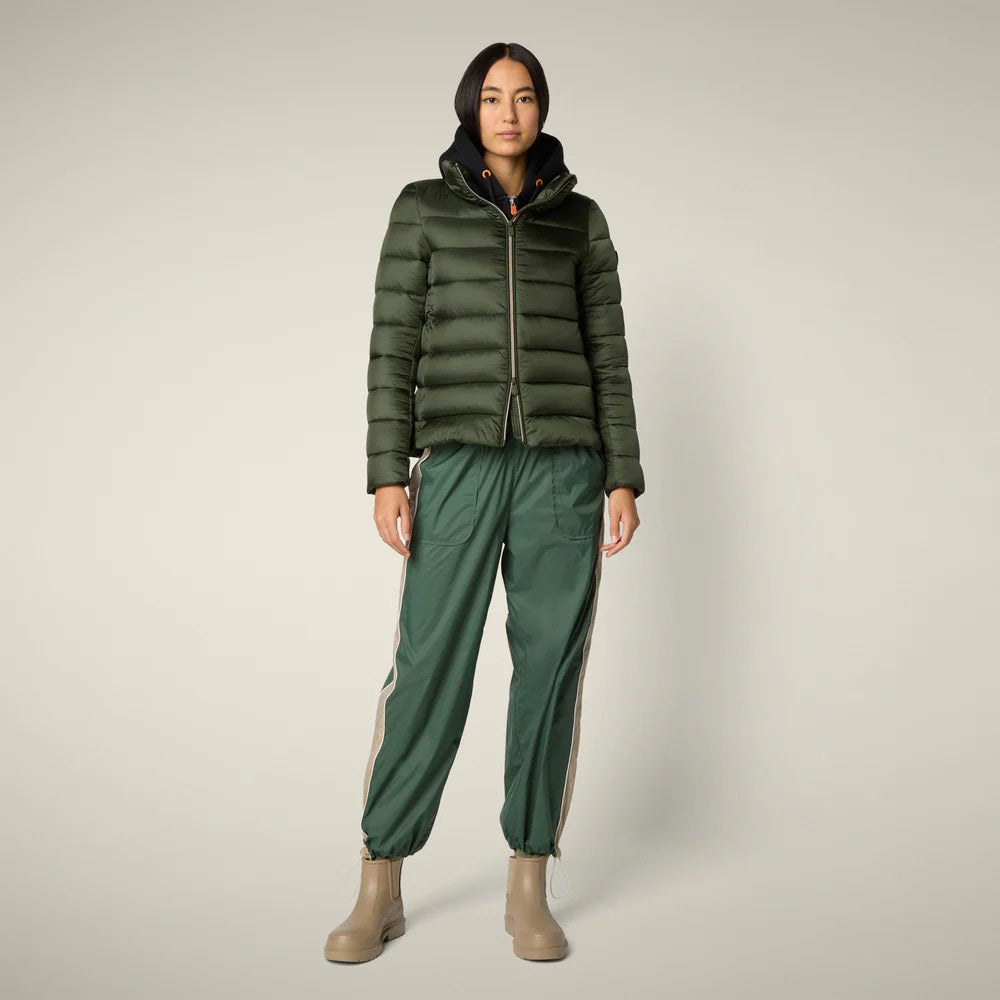 A person stands facing away in the SAVE THE DUCK - ELSIE PUFFER JACKET by SAVE THE DUCK, paired with loose green pants and tan boots against a plain light background.