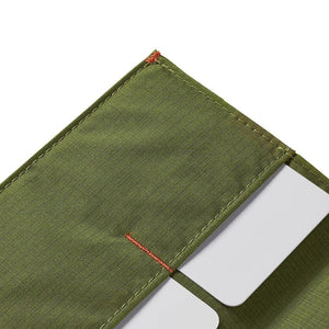 A Cala Green ALLETT RFID-blocking nylon wallet rests on a wooden surface beside a green notebook, portable stove, headlamp, black bag, pocket knife, camping gear, and round dark objects.