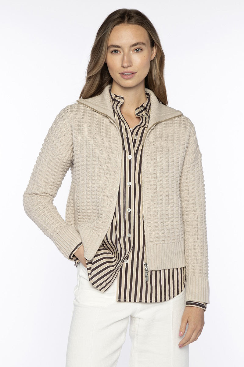A woman with long brown hair wears the KINROSS CASHMERE Bobble Knit Cotton Cardigan over a black-and-beige striped button-up shirt and white pants, standing against a plain white background with one hand in her pocket.