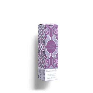 A clear 30ml ROSE ET MARIUS - A ROSE WINE UNDER THE ARBOR Eau de Parfum spray bottle, with a pink and white patterned cap beside it, rests on a white background. Soft light casts a gentle shadow to the left.