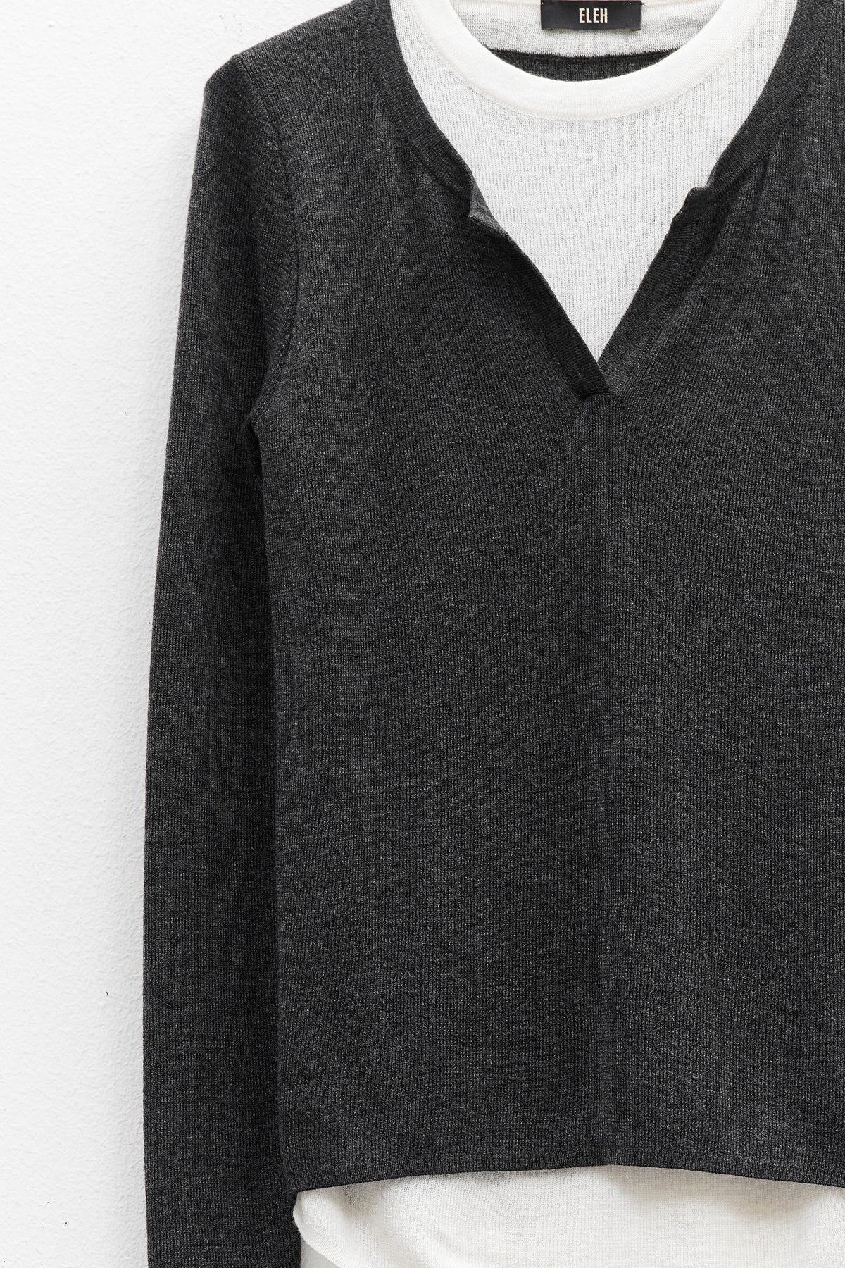 The ELEH - SWEATER WITH BUILT IN T-SHIRT features a charcoal gray sweater with a V-notch neckline layered over an attached white round-neck shirt, both displayed against a plain white background.