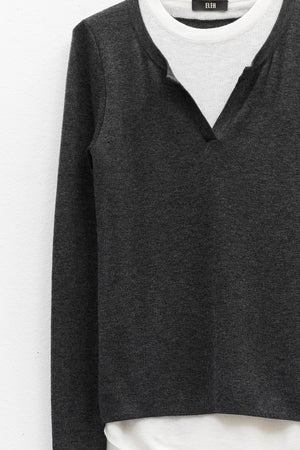 The ELEH - SWEATER WITH BUILT IN T-SHIRT features a charcoal gray sweater with a V-notch neckline layered over an attached white round-neck shirt, both displayed against a plain white background.