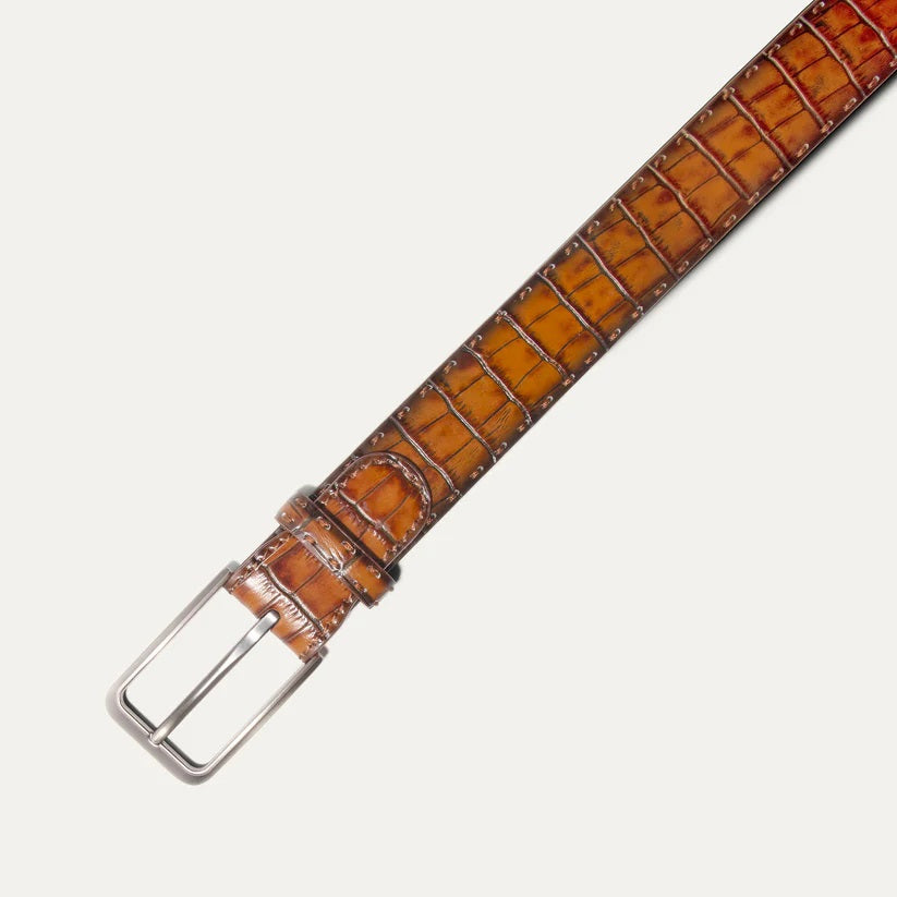 The WILL LEATHER GOODS - CROCO BELT IN COGNAC features Italian leather with a crocodile pattern and a silver buckle, shown coiled loosely on a light background.