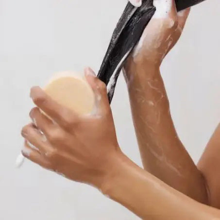 A round, beige solid conditioner bar sits on its light gray packaging labeled "KITSCH Coconut Repair Deep Conditioning Bar Mask." Infused with coconut oil for softness and shine, it detangles and conditions. The package highlights "Color Safe," "pH Balanced," "Vegan," and plastic reduction.