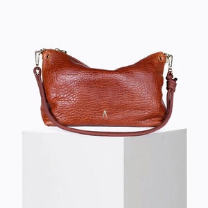A CRAIE STUDIO - MALLOW BUBBLE CLAY HANDBAG, crafted from vegetable-tanned lambskin with a textured brown bubble leather finish, features a gold clasp and a knotted strap. The handbag is displayed on a white pedestal against a plain background.