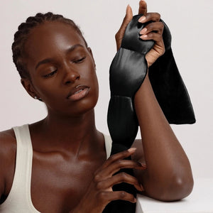 The NODPOD Silk Weighted Sleep Eye Mask in Noir by NODPOD is a dark blue, segmented eye mask featuring a strap-free design and unique four-pad shape. Text highlights its calming effect for stress relief and relaxation, all set against a light background.
