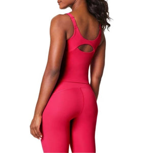 A woman wears the SPANX POWER BOOST SHELF TANK in bright pink with matching leggings, standing with her arms relaxed at her sides against a white background.