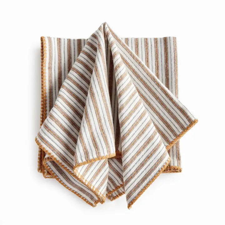 Elevate your table linens collection with the NAPA HOME AND GARDEN - SUTTON DINNER NAPKIN. This folded cotton napkin, featuring brown, white, and gray vertical stripes accented by decorative brown stitching along the edges, offers a stylish soft ochre touch—perfect for bringing both elegance and versatility to any dining setting. Displayed against a crisp white background, it’s a standout piece from NAPA HOME AND GARDEN.