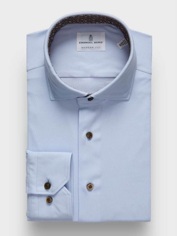 The EMANUEL BERG Flex Stretch Knit Shirt in Light Blue features brown buttons and a modern fit label inside the collar. Crafted from four-way stretch fabric, it is shown neatly folded against a plain light background.