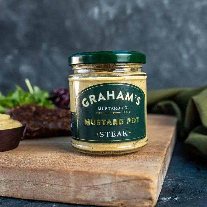 A jar of GRAHAMS - IRISH STEAK MUSTARD is shown. The label displays the brand name &quot;GRAHAM&#39;S&quot; and notes the company was established in 2014. The mustard has a creamy yellow color, perfect as a steak accompaniment, and is contained in a clear jar with a black lid.