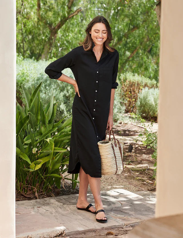 The dress is a FRANK &amp; EILEEN RORY Maxi Shirtdress in Famous Denim Black. It has a collar, rolled-up sleeves, a single chest pocket on the left side, and a curved hem. Crafted from fine Italian cotton, it is displayed against a plain white textured background.