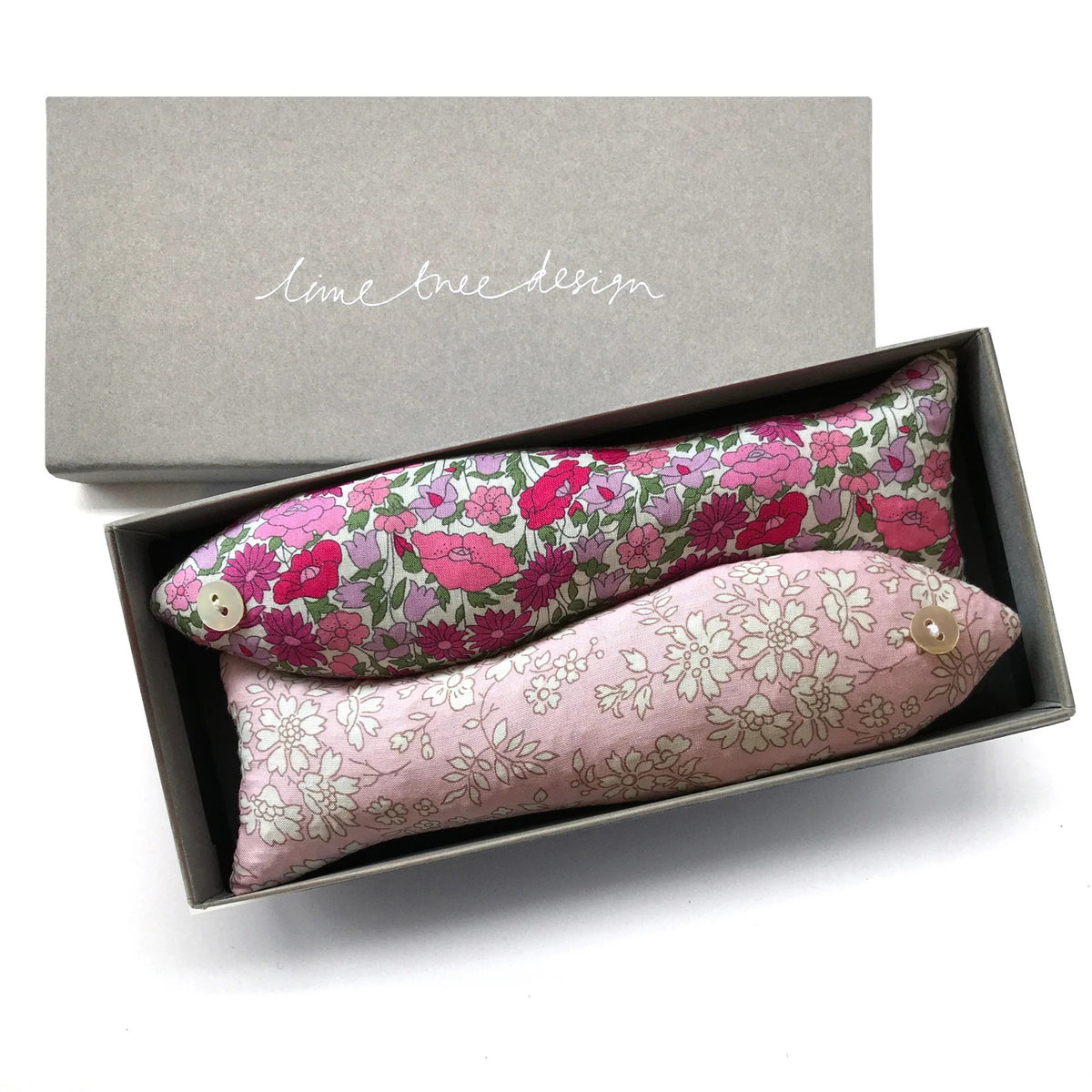 A box from &quot;LIME TREE COLLECTION LTD&quot; containing two LAVENDER FISH AND LITTLE PRINCESS SACHETs made from Liberty Tana Lawn fabrics. One is covered in a pink floral pattern, and the other has a white floral pattern on a light pink background. Both have button eyes.