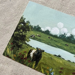 Bring home the charm of the countryside with the SOPHIE WYATT STUDIO - WILD MEADOWS & BELTIES ART PRINT, 11X14. This fine art print by SOPHIE WYATT STUDIO features a scenic green landscape with a pond, trees, colorful flowers, and Belted Galloway cows under puffy white clouds on linen fabric.