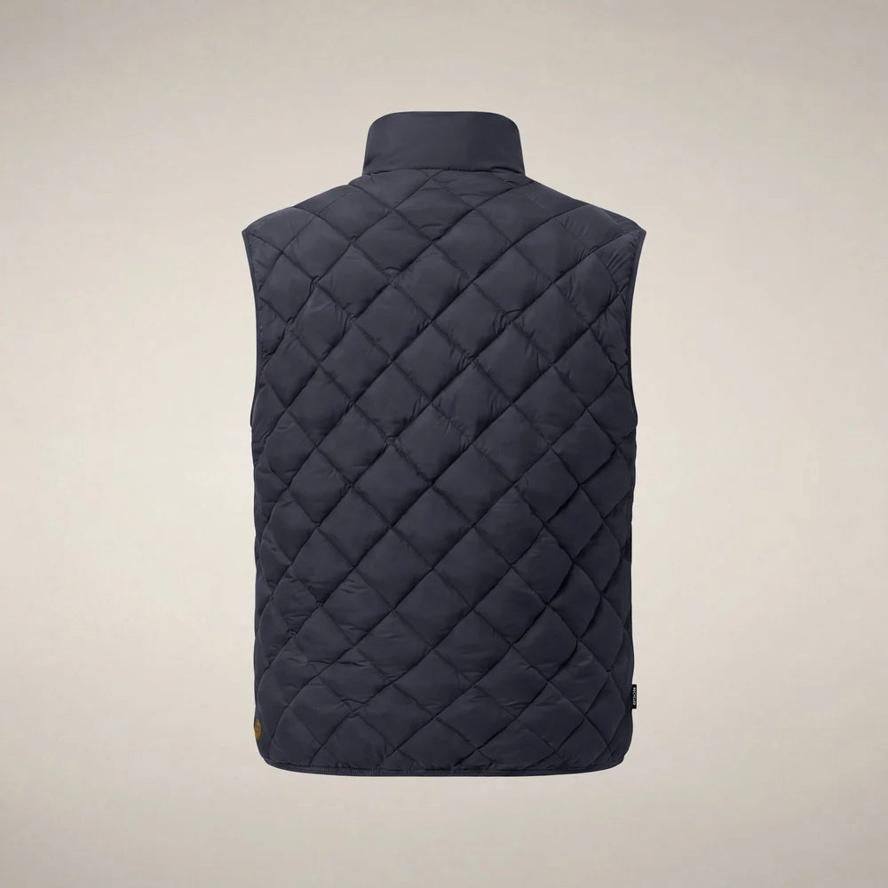 A person stands facing forward, wearing the SAVE THE DUCK - FABRICE Puffer Vest in Blue Black from SAVE THE DUCK, featuring recycled Plumtech insulation, layered over a black long-sleeve shirt and gray pants. They have a neutral facial expression and are posed against a plain white background.