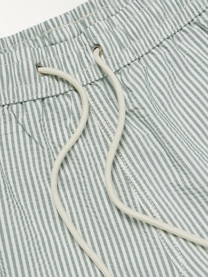 A person wearing HARTFORD - SEERSUCKER SWIM TRUNKS IN GREEN with an elastic waistband and drawstring stands against a plain light background.