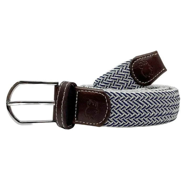 A person in a light blue polo, beige shorts, and a white golf glove grips a club on grass, accessorized with the ROOSTAS - RIVIERA WOVEN STRETCH BELT by ROOSTAS for added comfort during play.