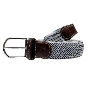 A person in a light blue polo, beige shorts, and a white golf glove grips a club on grass, accessorized with the ROOSTAS - RIVIERA WOVEN STRETCH BELT by ROOSTAS for added comfort during play.