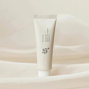 A white skincare tube with black text and red accents, featuring a secured cap, provides a minimalistic, elegant design. GLOWISS's BEAUTY OF JOSEON - RELIEF SUN RICE SPF50 offers lightweight sun protection. The background is plain white.