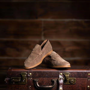 COLLARS AND CO's Sigaro Penny Loafers in dark tobacco suede are men's slip-on loafers with low heels, rubber soles, and a decorative strap across the top, shown against a white background.