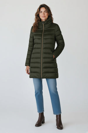 A woman in the SAVE THE DUCK - LYDIA PUFFER COAT by SAVE THE DUCK, paired with a white dress, maroon knee-high boots, and holding a fluffy light pink clutch, stands against a plain beige background.