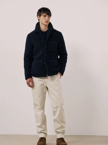 A young person with short dark hair wears the HARTFORD - Sherpa Utility Jacket in Navy by HARTFORD over a black shirt, looking directly at the camera against a plain light background. This warm sherpa layer brings both comfort and style to casual menswear.