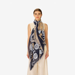 A woman, her face partially visible from the nose down, wears a sleeveless cream top and the INOUI EDITIONS - OCTOPUS SCARF IN NAVY by INOUI, featuring intricate hand-printed designs and text elegantly tied around her neck.