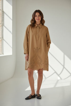 A person stands against a white background wearing the MEIMEIJ Lasercut Cotton Shirt Dress featuring eyelet embroidery and scalloped cuff hems, paired with black flat shoes.