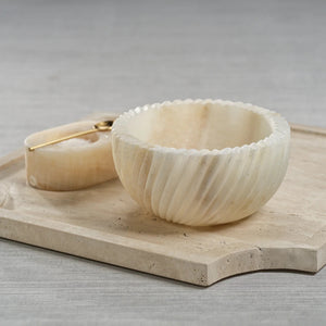 The SPIRALED ONYX SERVING BOWL by ZODAX features a round, off-white design with a grooved exterior and is crafted from elegant Onyx Marble, shown against a white background.
