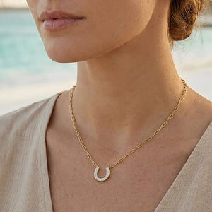 Introducing the ELLA STEIN - LUCKY HORSE SHOE PENDANT NECKLACE by ELLA STEIN, a gold-plated stainless steel necklace featuring a horseshoe-shaped pendant accented with small, sparkling white stones on one side—an elegant piece that captures the timeless allure of fine jewelry.