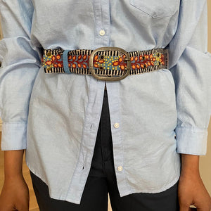 The JENNY KRAUSS - GROWING SEASON BELT by JENNY KRAUSS is a coiled, handcrafted Peruvian belt with black and white stripes, red and yellow leaf and dot embroidery, silver metal buckle, shown on a white surface.