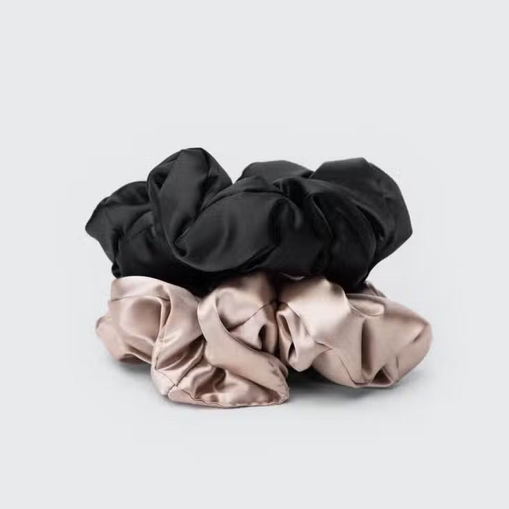 Two satin scrunchies are stacked against a light gray background. These KITSCH - SATIN SLEEP PILLOW SCRUNCHIES, in black and beige, offer a smooth, shiny texture ideal for frizz-free styling and breakage prevention.