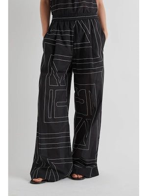A person in profile wears the MEIMEIJ ABSTRACT PRINT PANT, featuring an elastic waistband and wide-leg silhouette, styled with black sandals against a plain light background.