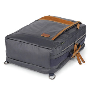 The TSD BRAND - MADRONE COATED CANVAS BACKPACK IN NAVY features brown leather accents, a spacious main compartment, a padded laptop sleeve with snap closure, and multiple zippered pockets on the inside flap.