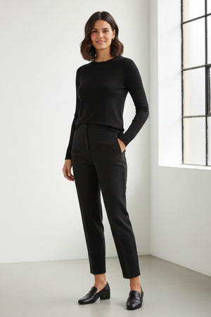 A woman stands facing forward, smiling softly with her hands by her sides, wearing the KINROSS CASHMERE Sequin Crew Neck Sweater in light gray and black pants against a plain white background.