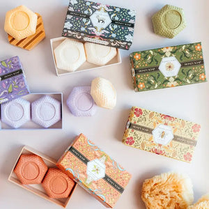 Experience the BAUDELAIRE Orange Blossom Honey Soap 3.5 oz, 2 Bar Gift Box—a beautifully presented set featuring two hexagonal orange soaps nestled in an open decorative box adorned with floral designs and a central bee illustration. This triple-milled soap by BAUDELAIRE offers a luxurious lather and a delicate orange blossom honey fragrance, making it an ideal indulgence for yourself or a thoughtful gift for someone special.