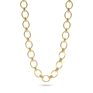 A person in a white blouse displays the CAPUCINE DE WULF - CLEOPATRA GRANDE LINK NECKLACE, made of 18K gold with circular links. Their hands feature gold rings, emphasizing the handmade jewelry's elegance.