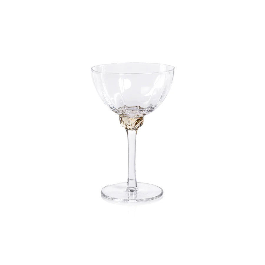Introducing the MARTINI COCKTAIL OPTIC GLASS by ZODAX: a clear, elegant stemmed glass featuring a shallow, wide bowl. The glass boasts a detailed, decorative stem and a circular base. With a 150 ml capacity, its minimalist and sophisticated design is ideal for serving champagne or cocktails.