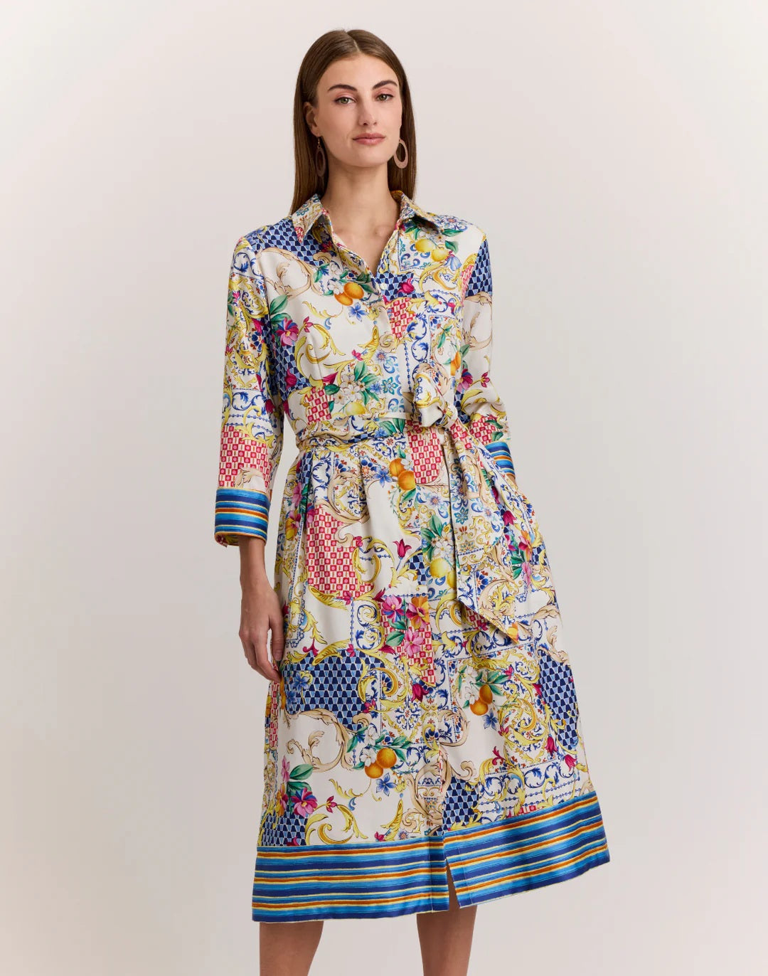 A woman in the HINSON WU Robin 3/4 Sleeve Dress in Amalfi Print—featuring vibrant blue, yellow, red, and white floral and geometric patterns—stands against a plain background.